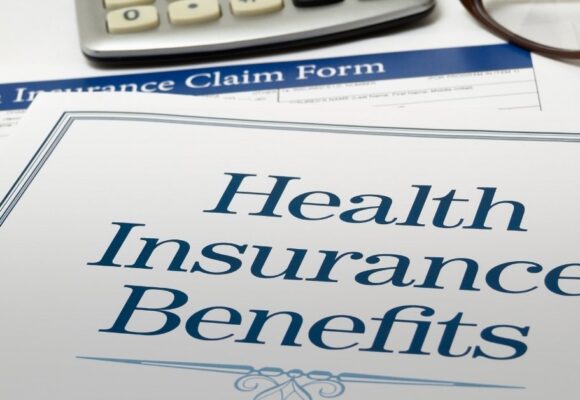 Image of a desk with a paper that says 'Health Insurance Benefits' and glasses with a calculator