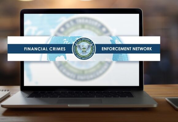 Image of a desk with a laptop, the screen has the FinCEN logo
