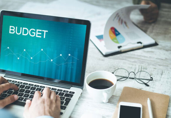 Image of a desk with devices and coffee and a laptop that says 'Budget'