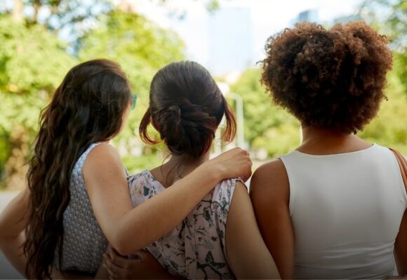 A trio of women, outdoors, with their backs turned to us
