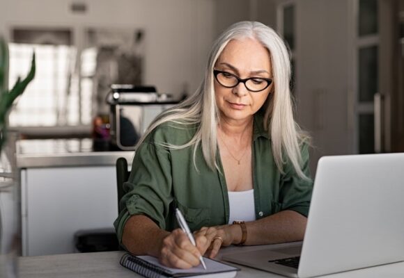 Image of a mature woman working at a laptop with pen and paper