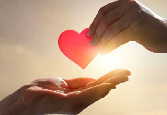 Image of one hand giving another hand a red heart